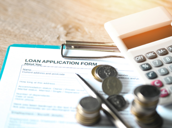 A loan application form placed on a table alongside scattered coins and a calculator, symbolizing financial planning and access to credit through NBFCs using Finpage's lending software.